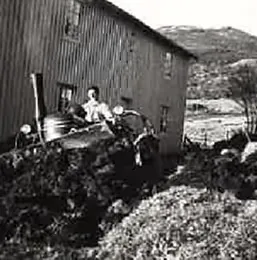 Traktor foran et trehus i ulendt terreng