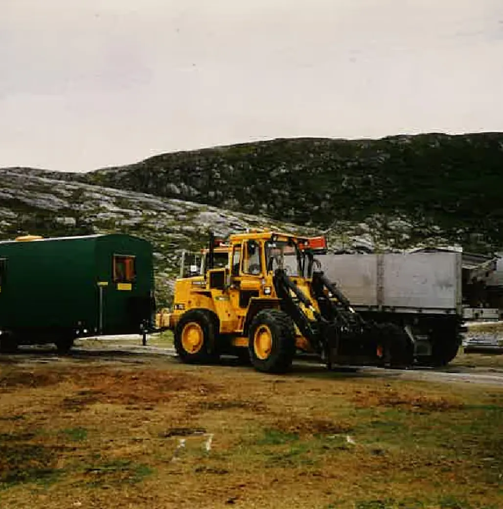 Gul hjullaster ved en brakke og en container