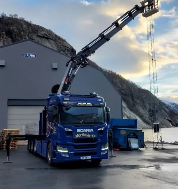 Blå Scania-lastebil fra Terje Halsan med kran, foran en lagerhall i Glomfjord