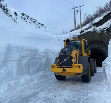 Gul hjullaster på en brøytet vei mellom høye snøvegger