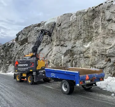 Volvo-gravemaskin med tilhenger ved en fjellskjæring