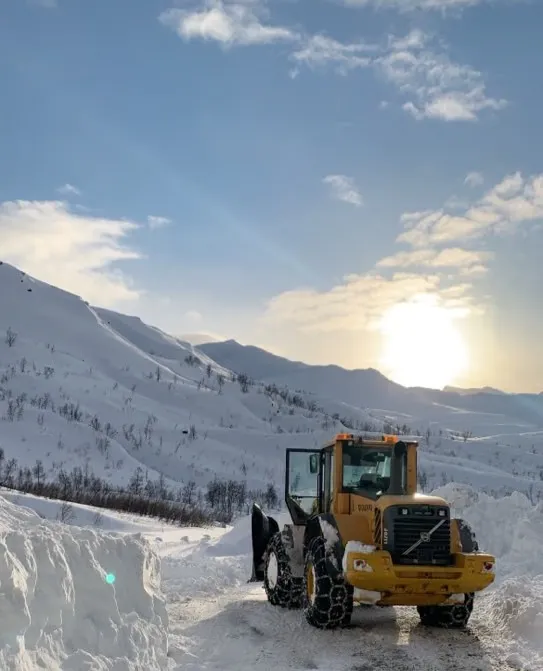 Gul Volvo-hjullaster med kjetting på en brøytet fjellvei i motlys