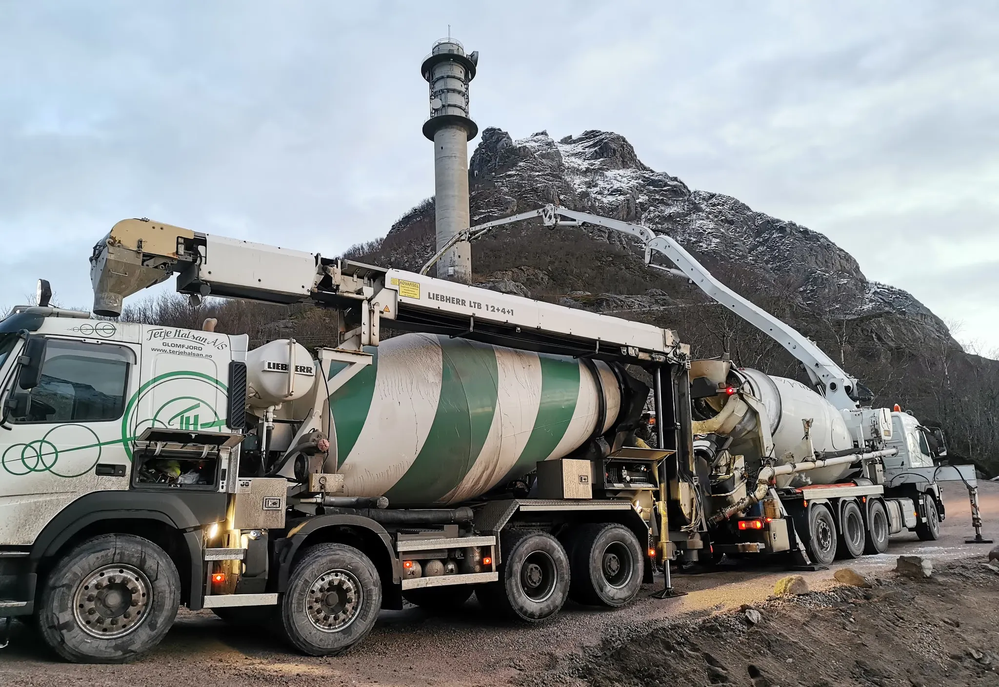 Betongbil og betongpumpe som støper ved et tårn under et fjell