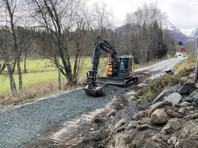 Gravemaskin som legger grus på en gårdsvei mellom trær