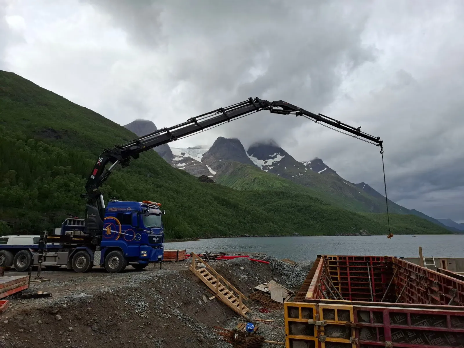 Blå kranbil som løfter ved forskaling på en byggeplass ved fjorden