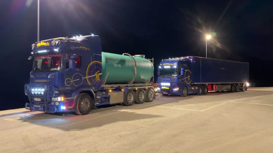 To blå lastebiler om natten, den ene med grønn tank og den andre med semitrailer