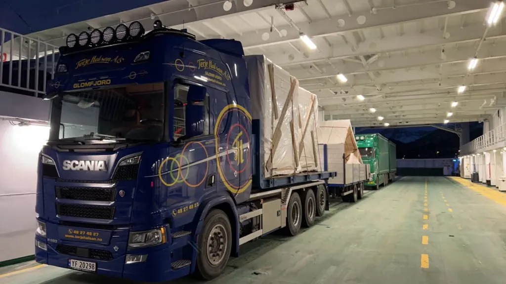Blå Scania-lastebil med last på henger på bildekket på en ferje