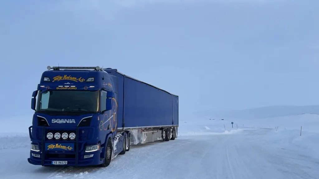 Blå Scania-trekkvogn med semitrailer på en snødekt fjellvei