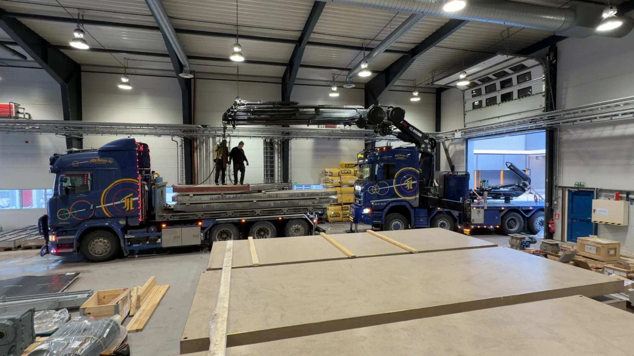 To blå kranbiler som losser materialer inne i en stor hall