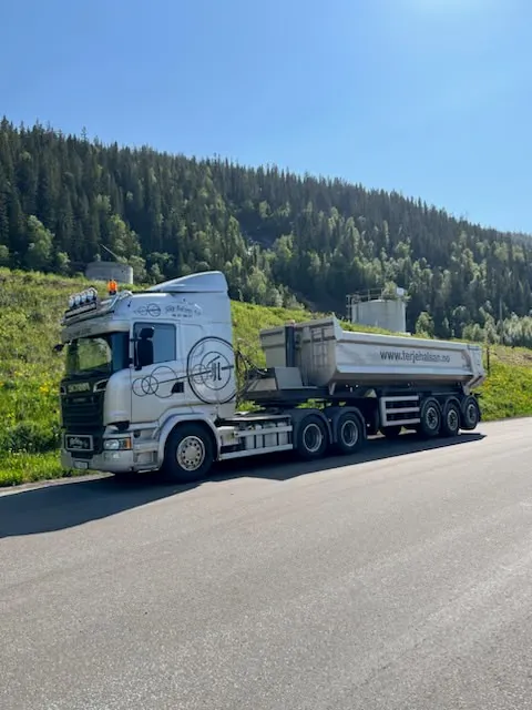 Hvit Scania-trekkvogn med tippsemitrailer på en vei en solrik sommerdag