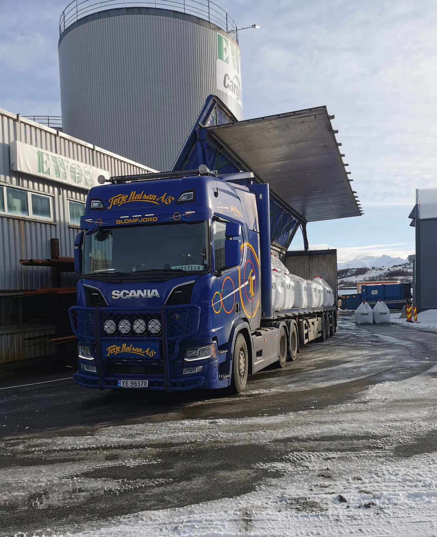Blå Scania-trekkvogn med semitrailer som lastes ved en fabrikk med silo