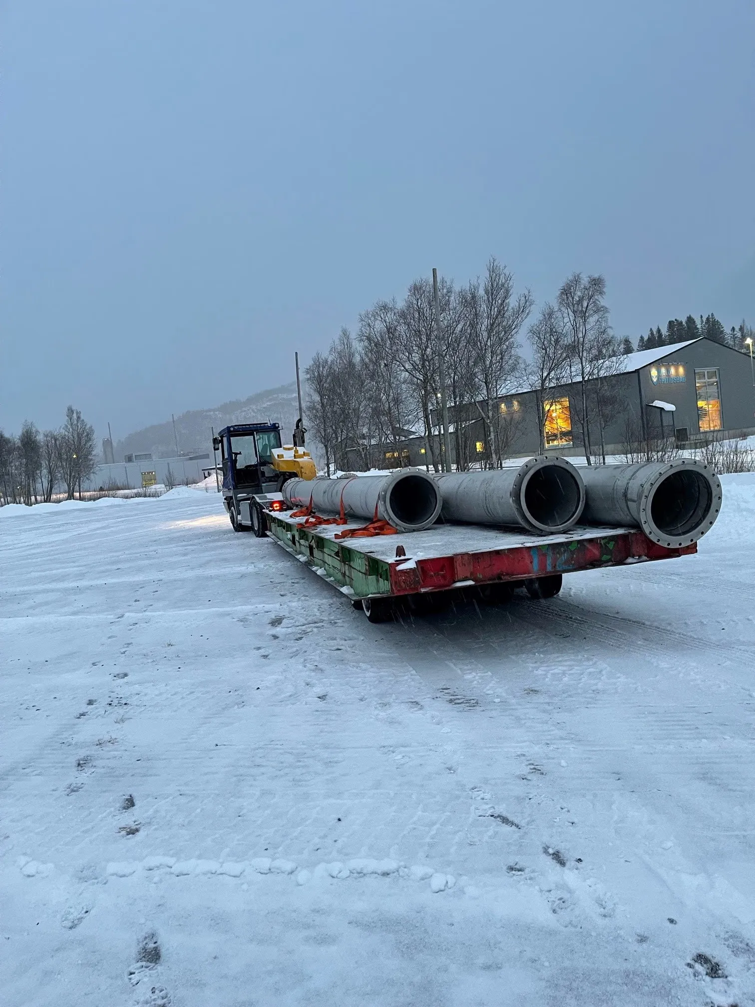 Lastebil med lav semitrailer lastet med store betongrør på en snødekt plass