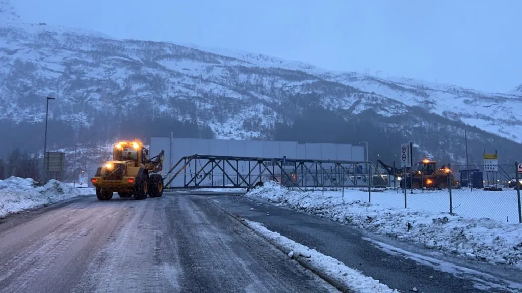 Hjullastere som frakter en lang stålkonstruksjon langs en snødekt vei
